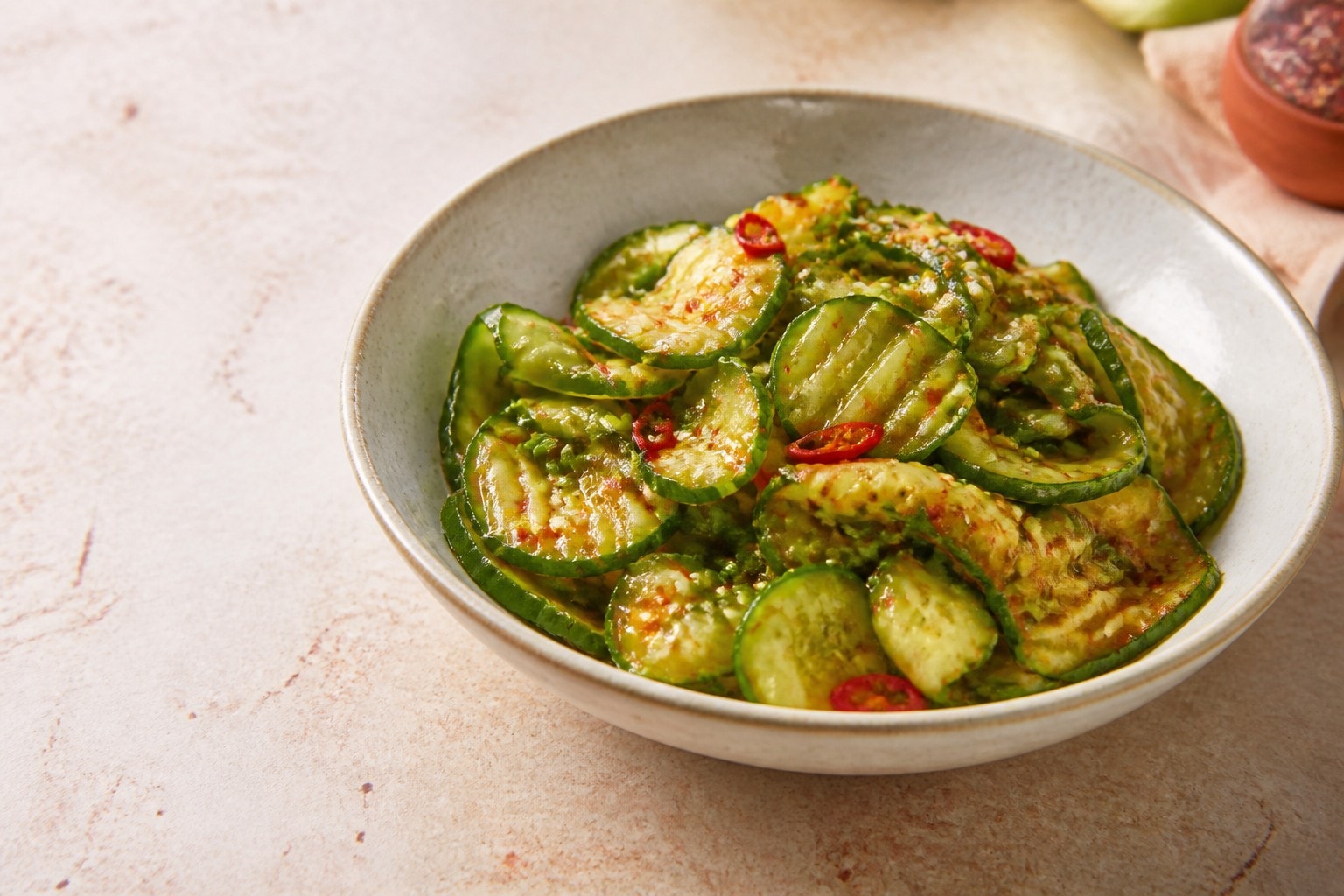 A bowl of crisp spicy cucumber salad with chili garlic dressing, sesame seeds, and scallions.
